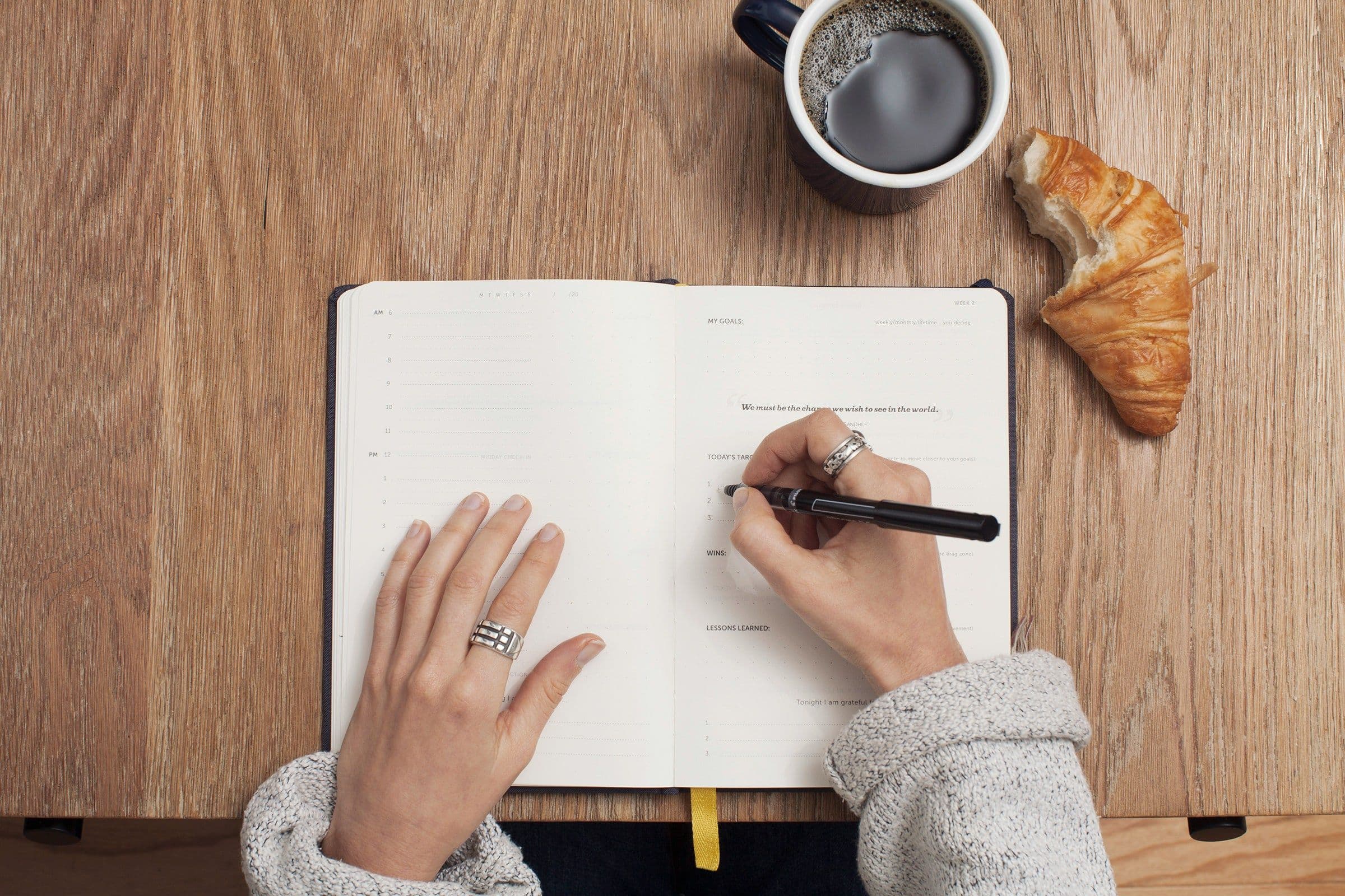 a woman's hand writing in a notebook with a cup of coffee